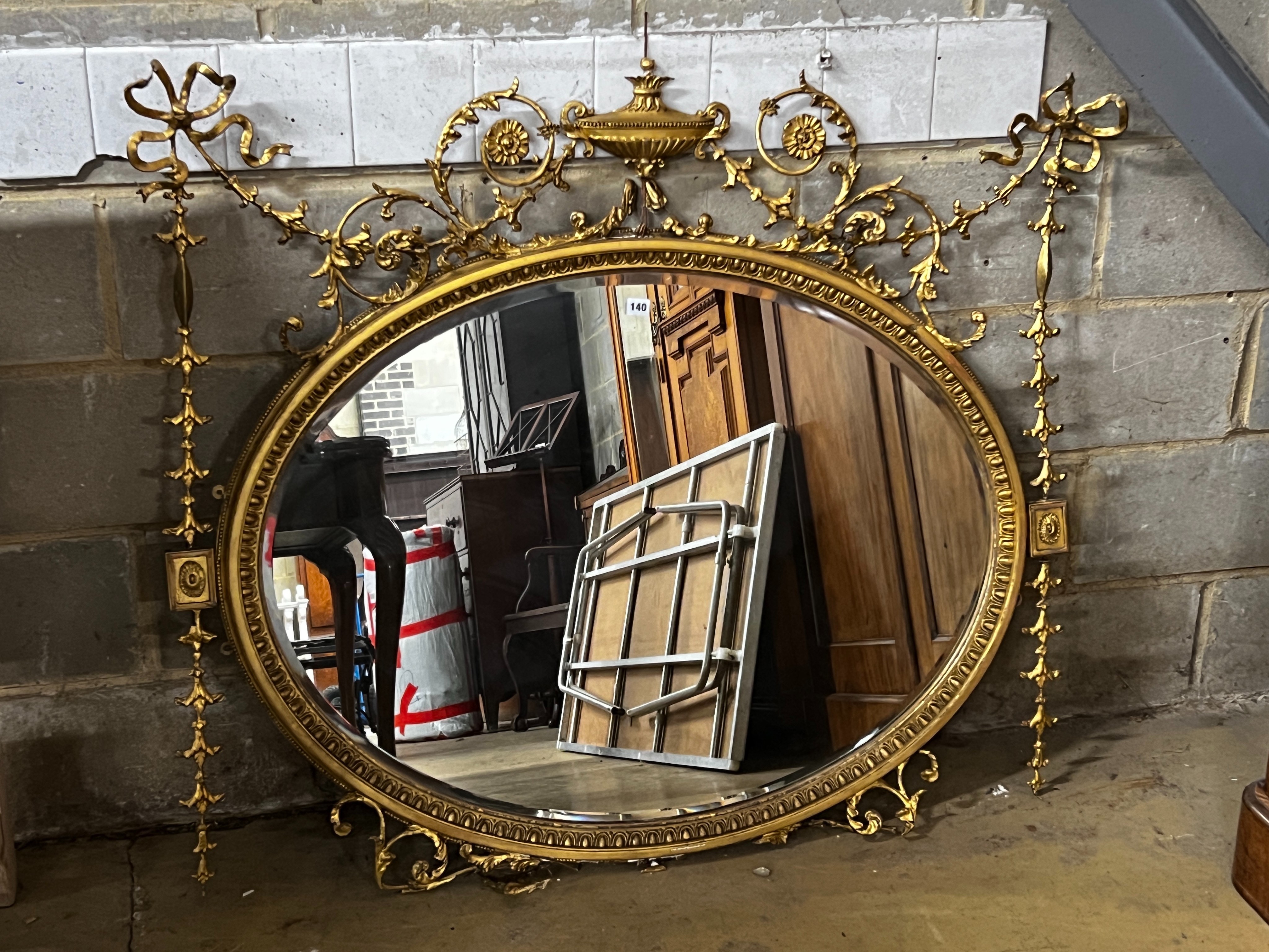 An Edwardian Sheraton revival oval giltwood and composition wall mirror in need of restoration, width 130cm, height 115cm